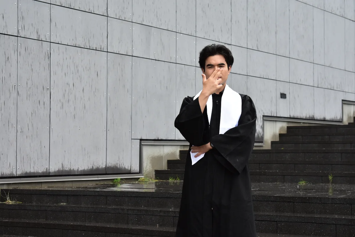 Mathew Neves in graduation robes, standing on outdoor steps.